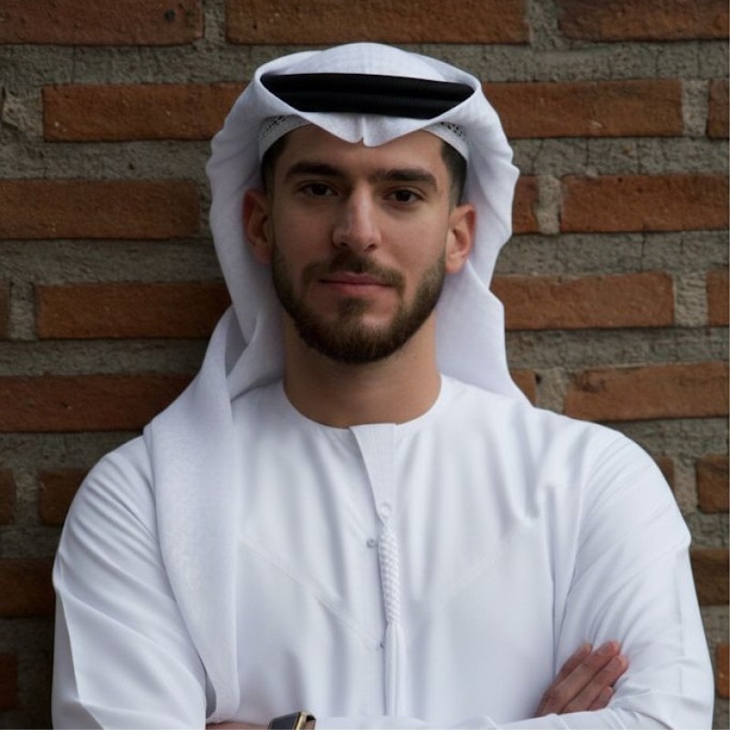 Mohammed Faez in a white kandura and ghutra, arms crossed, in front of a brick wall